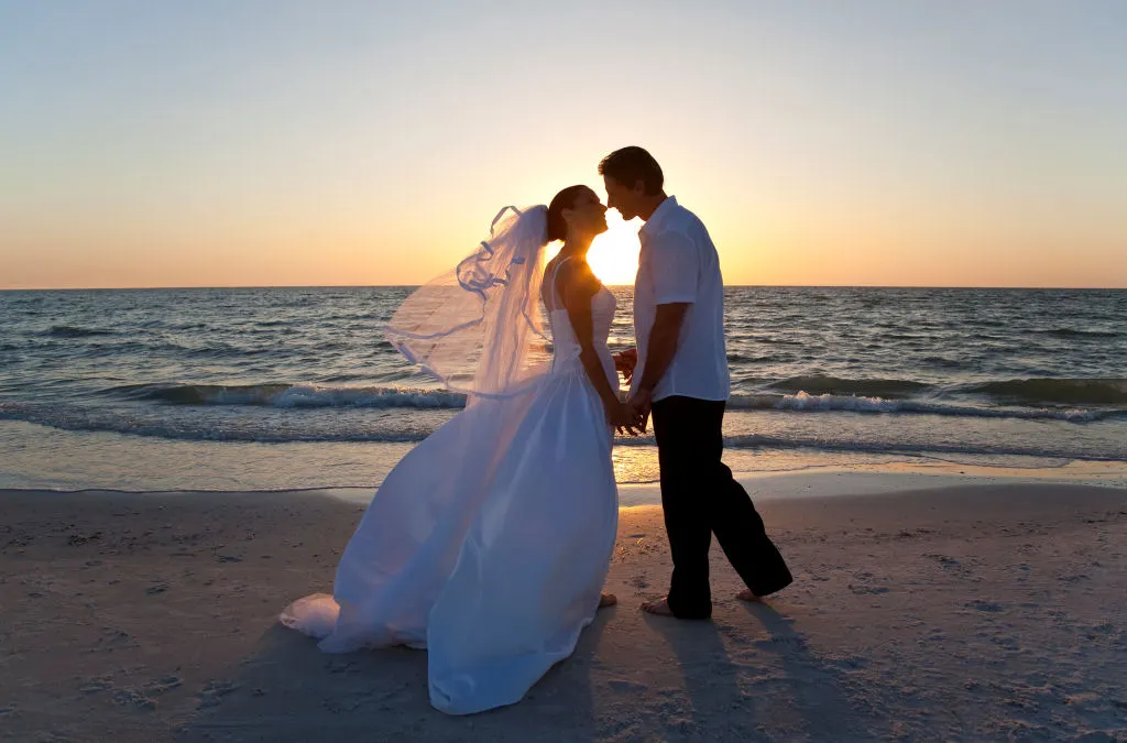 Man and woman kiss following marriage vows on the beach in New Buffalo.  A beautiful sunset as a backdrop